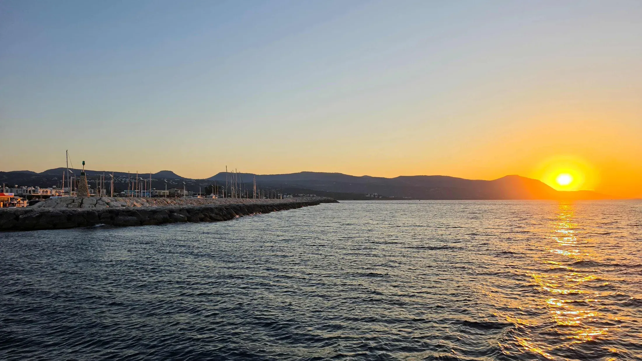 Die Sonne geht hinter dem Hafen von Latchi über dem Meer unter